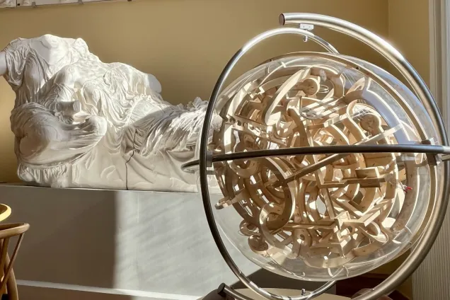A labyrinth in a glass globe in front of a white statue. Photo.