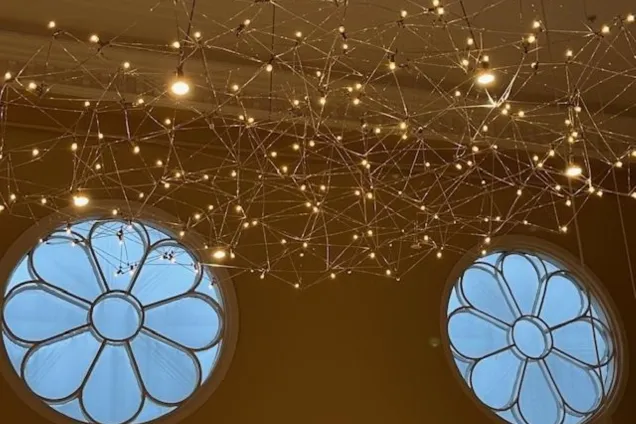 In front of two rosette windows: many small lamps formed as a net. Photo.