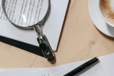 Magnifying glass and pens over papers with text. Photo.