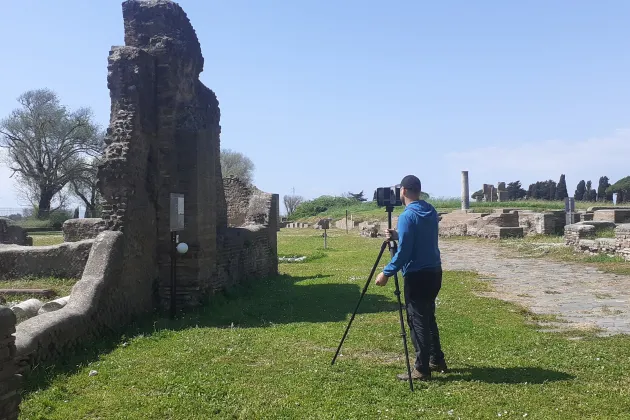 En person med kamera på stativ i en romersk ruin. Foto.